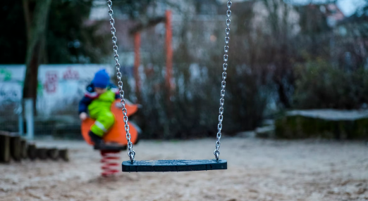 An image showing a swing in a park, with a child in the background