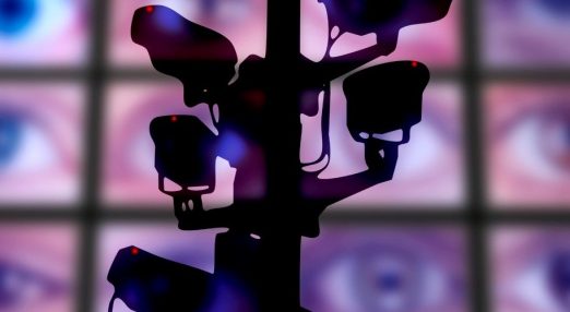 An image showing multiple surveillance cameras while in the background there are multiple screens showing close-up of eyes.
