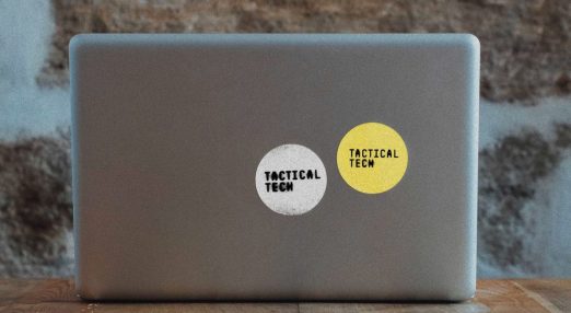 An image showing a laptop with 2 stickers with the Tactical Tech logo