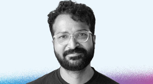 Black and white portrait of Amber Sinha against a light blue background. The background features a subtle gradient from blue to purple at the bottom.